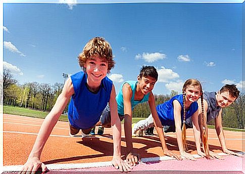 Children smile as they do push-ups on a running track.