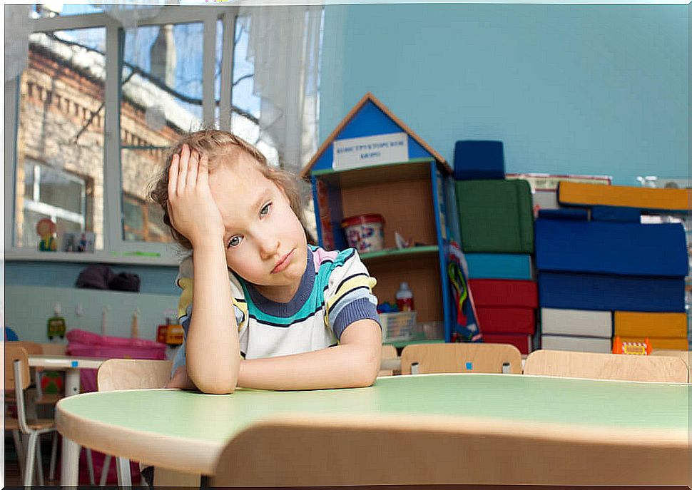 Girl sitting at a school table holds her head with a sad or frustrated expression.